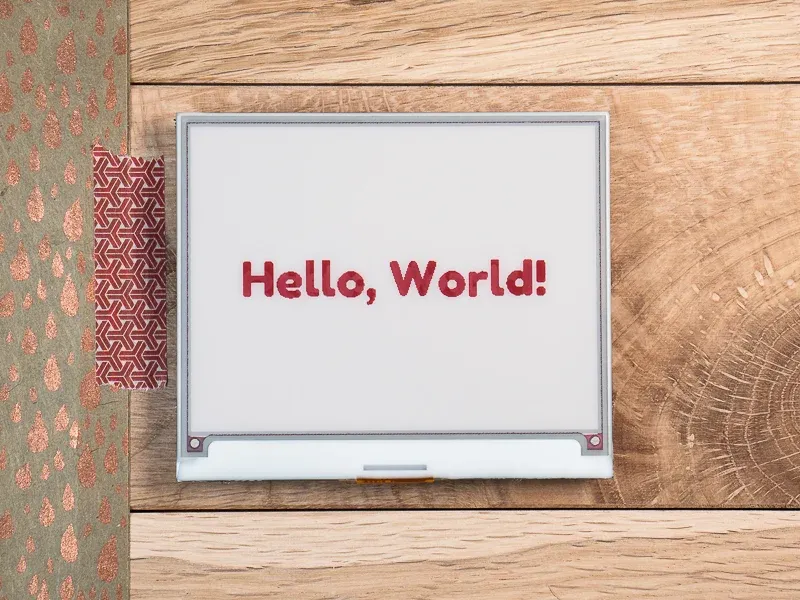 A Pimoroni InkyWhat on a table with the words "Hello, World!" on the screen.