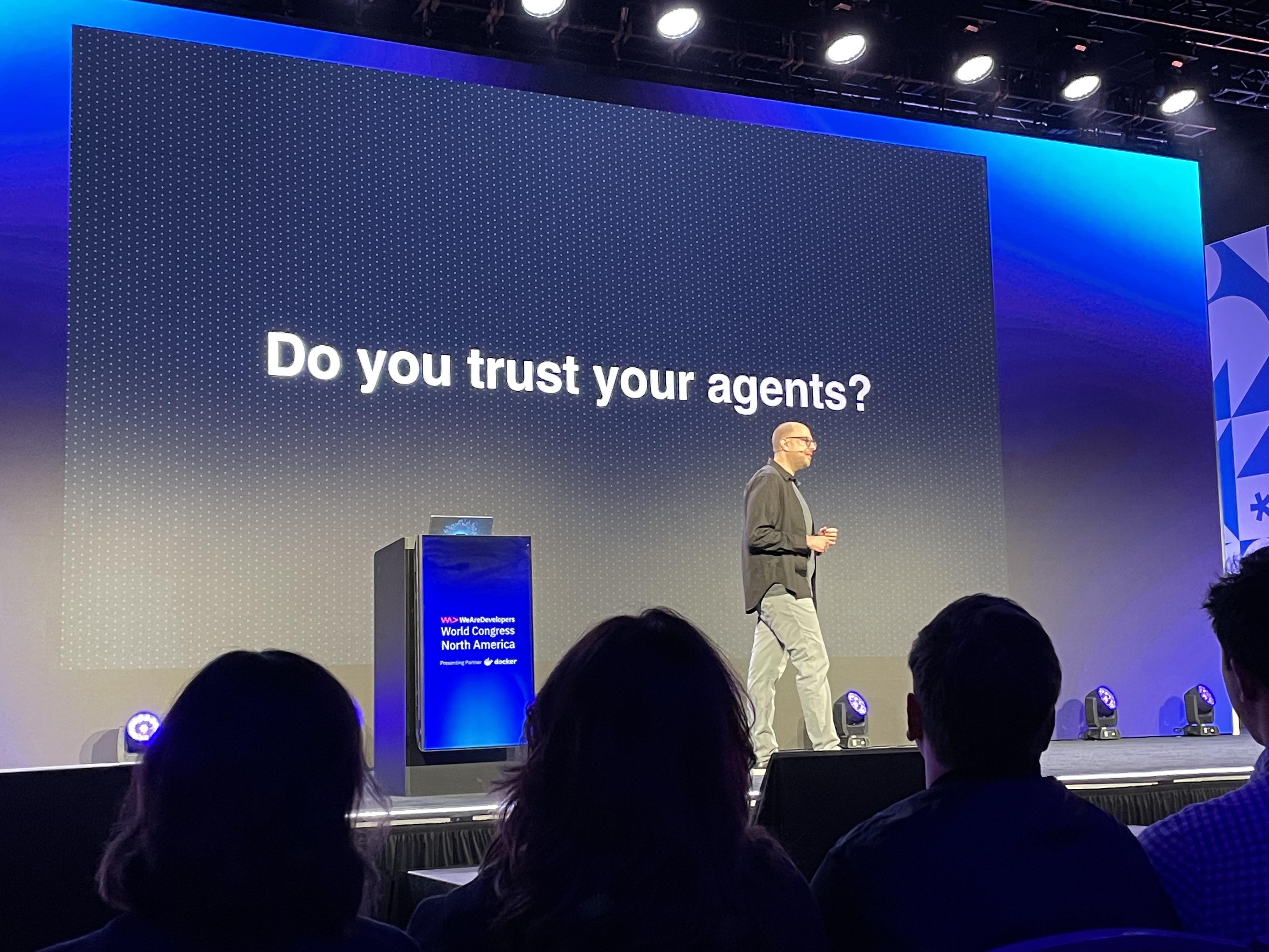Mark Cavage on stage in front of a screen with the words "Do you trust your agents?"